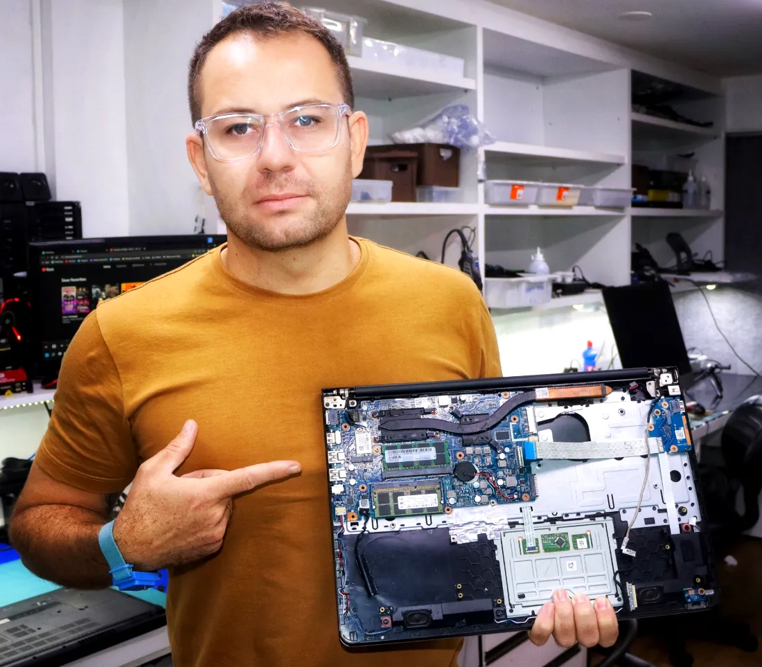 Erick Zenha, técnico da InfoZenha, na bancada segurando um notebook aberto para manutenção